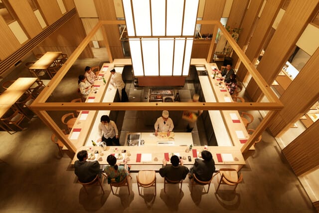 西村屋的室內照片，它的天花板很高，顯得氣派。座位有霸台與一般桌子，霸台可以看師傅料理食材