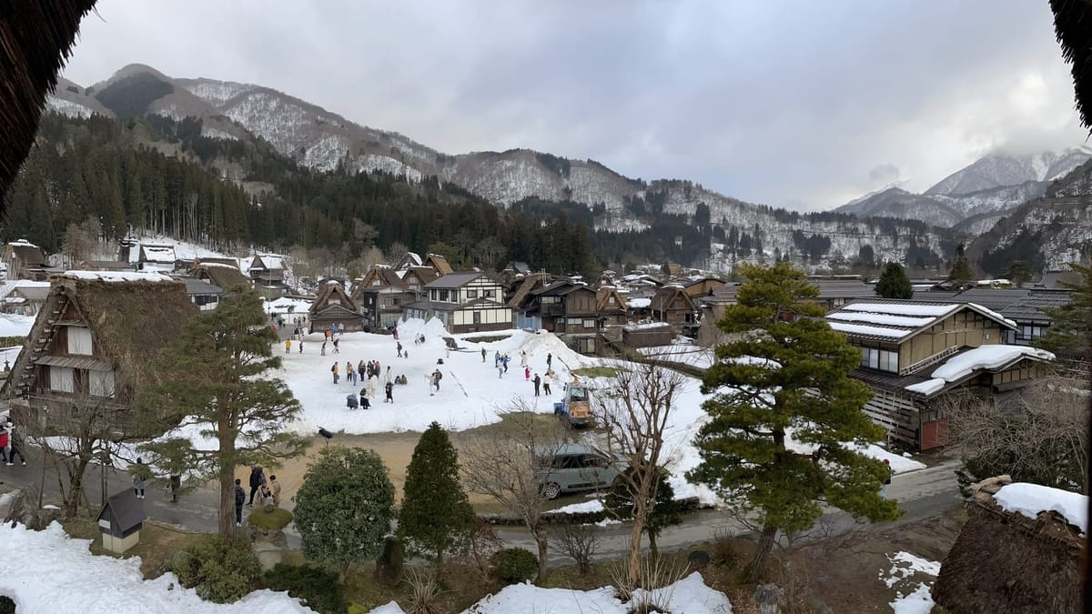 日本合掌村冬季雪景全貌，遠方是連綿山脈
